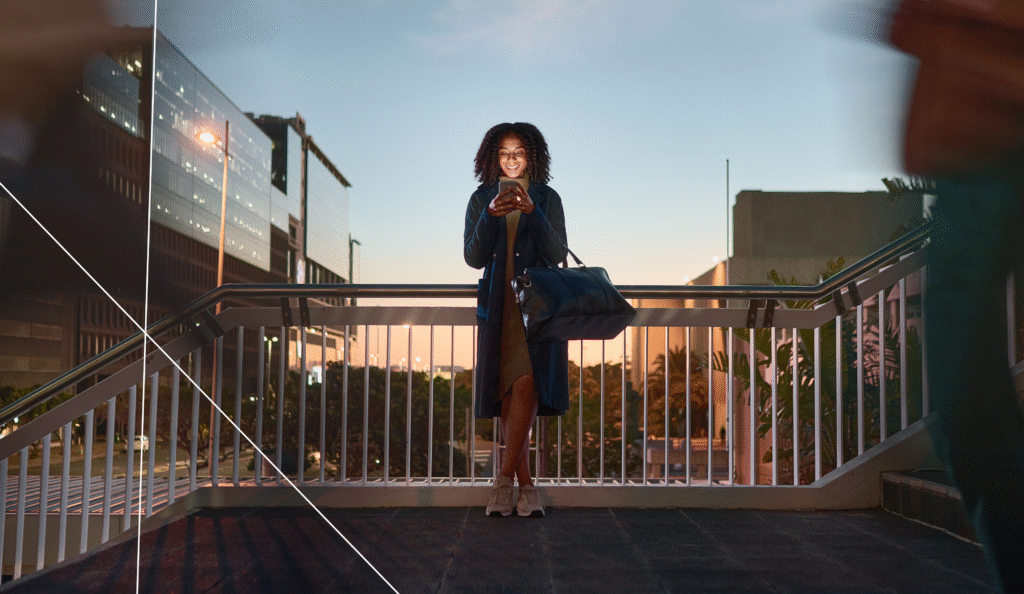 Woman using smartphone in the city at sunset, symbolizing digital citizen engagement and resilience technology for safer smart cities.