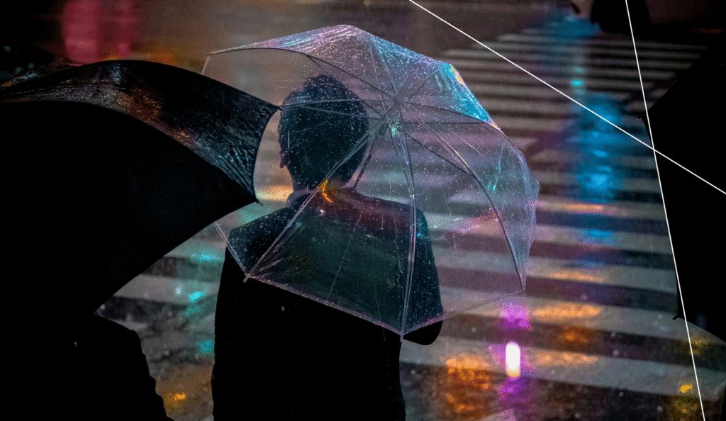 Person under a transparent umbrella crossing a rainy city street at night.