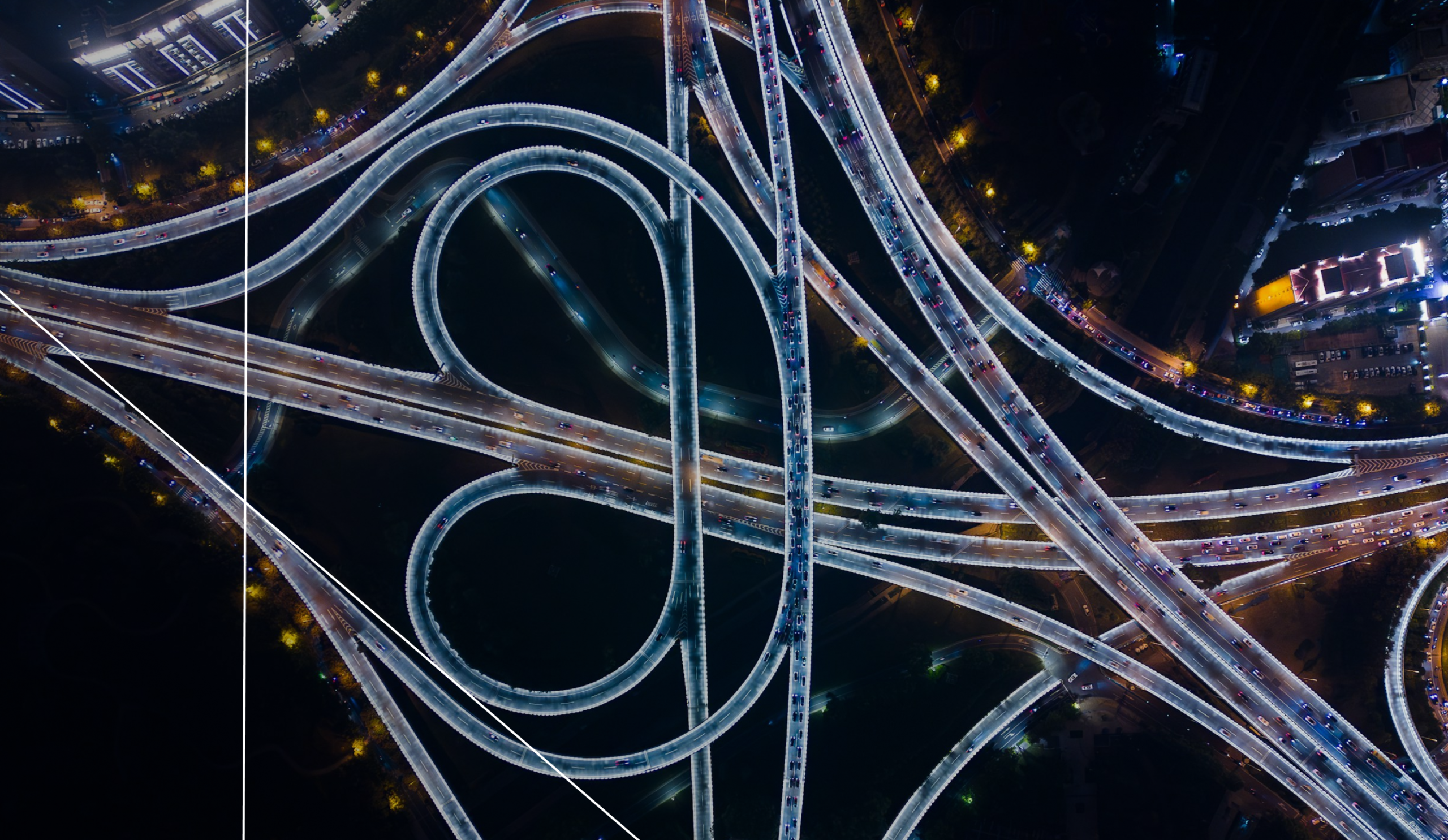 Aerial view of a complex urban highway interchange at night, illustrating the interconnected infrastructure and resilience required for modern smart cities operating in high-stakes environments.
